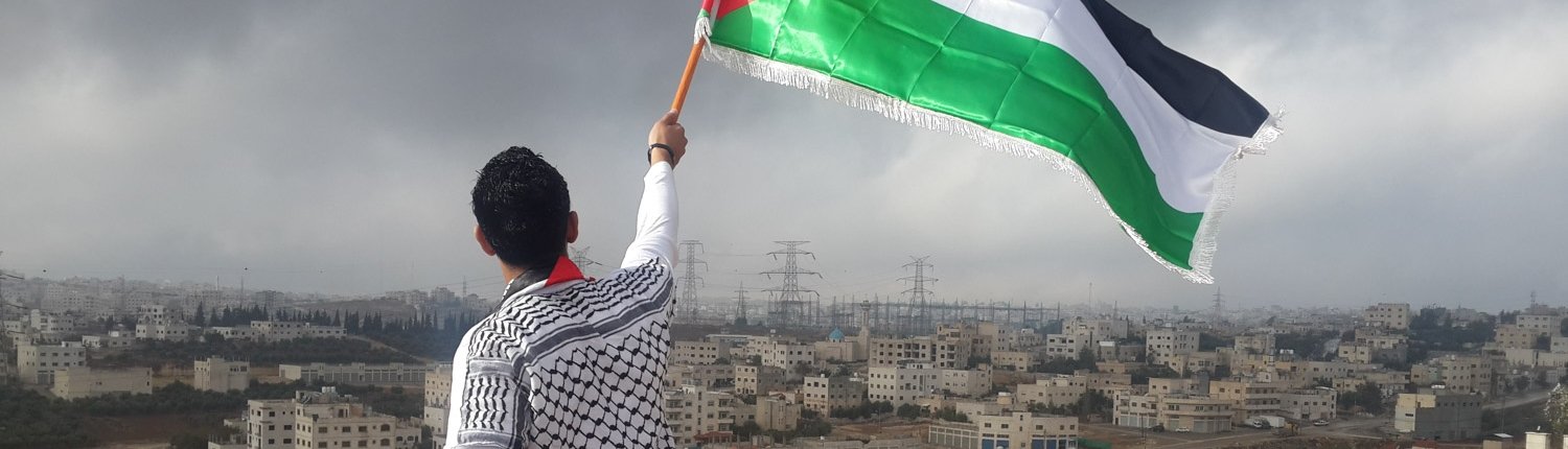 Vyras, laikantis Palestinos vėliavą. Tolumoje – miestas