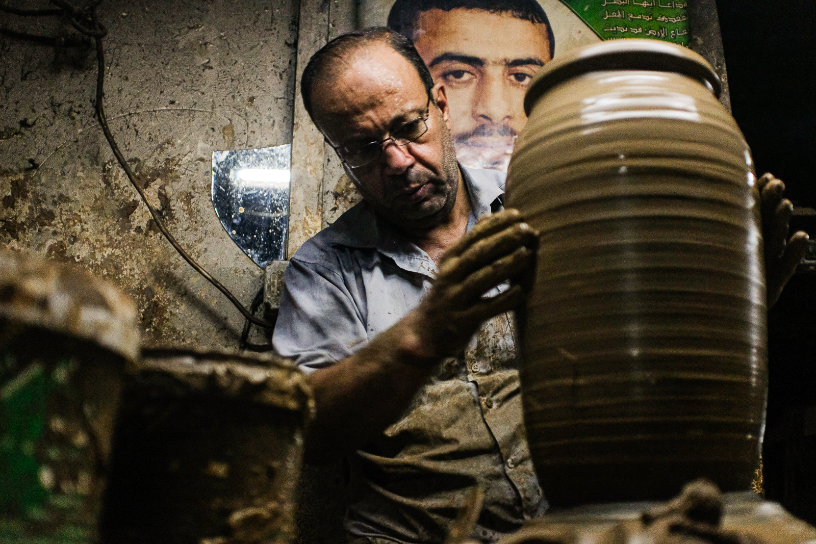 Žymiausiose ir seniausiose Gazoje keramikos dirbtuvėse. Dirbantis vyras, kuriam už nugaros kabo artimojo portretas, kurį pasiglemžė Izraelio režimas. Gaza, 2021 m. rugsėjo 29 d. Nuotrauka: Mahmoud Nasser.